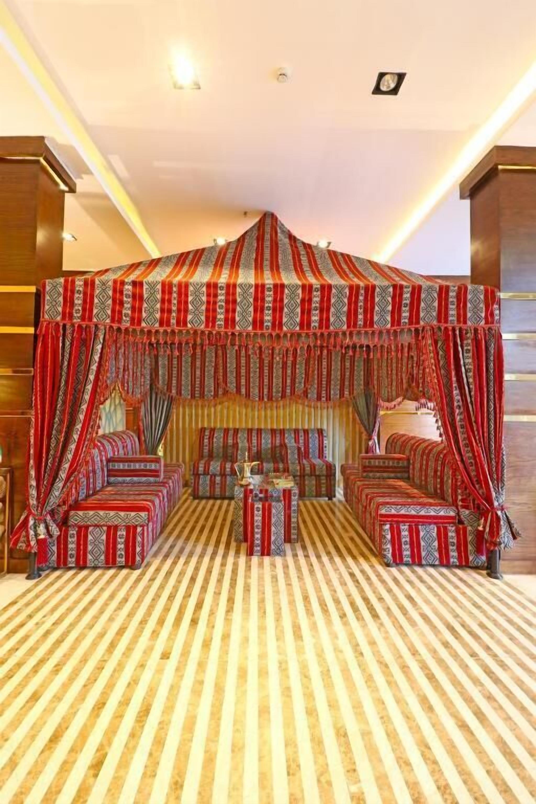 A room with a canopy bed, multiple seating options, and a patterned carpet.