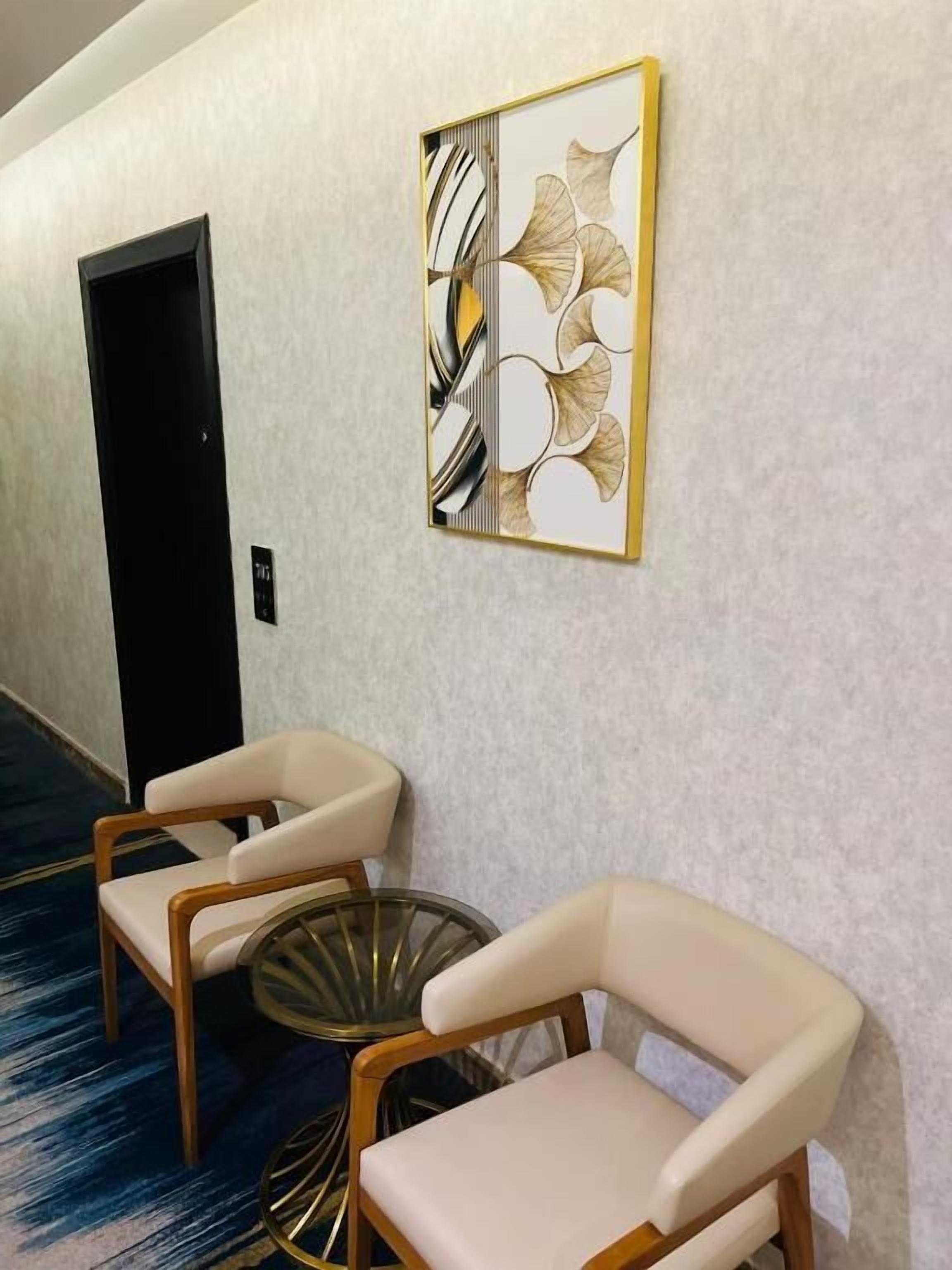 A hallway with two white armchairs and a glass coffee table, a decorative wall piece, and a door.