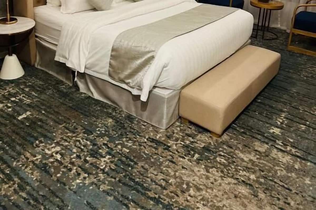 A hotel room with a large bed, a bedside table, a chair, and an air conditioning unit.