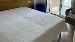 Een slaapkamer met een bed, een hanglamp van riet, een blauwe stoel en een schuifdeur die leidt naar een buitenruimte.