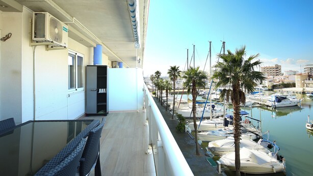 A balcony with a glass table and chairs, overlooking a marina with boats and palm trees. - V031 - Port Canigo, V031 - Port Canigo - Apartamento con piscina (Roses)