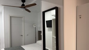A bedroom with a bed, a wardrobe, a mirror, a ceiling fan, and a TV.