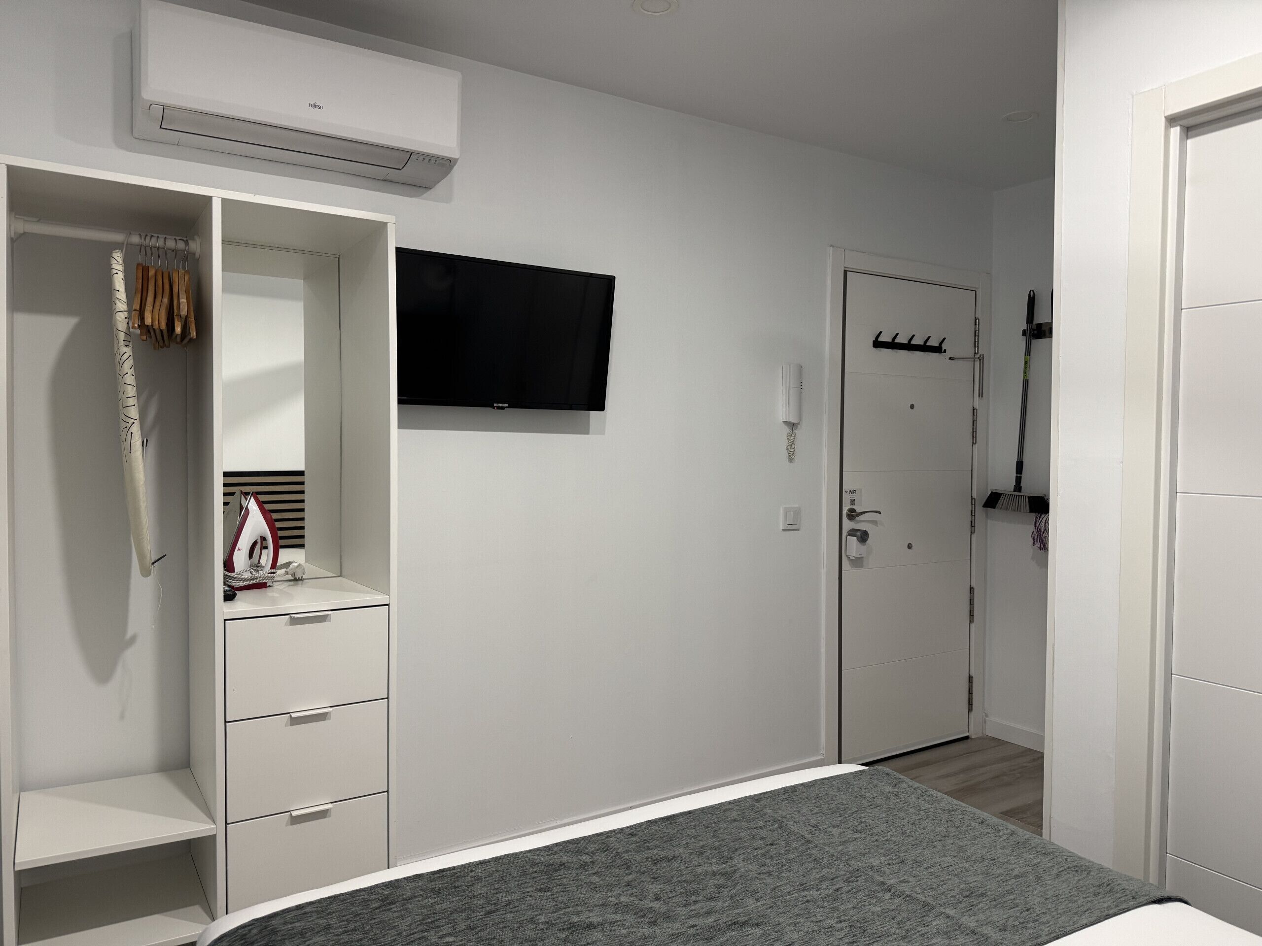 A bedroom with a bed, a wardrobe, a TV, and a door.