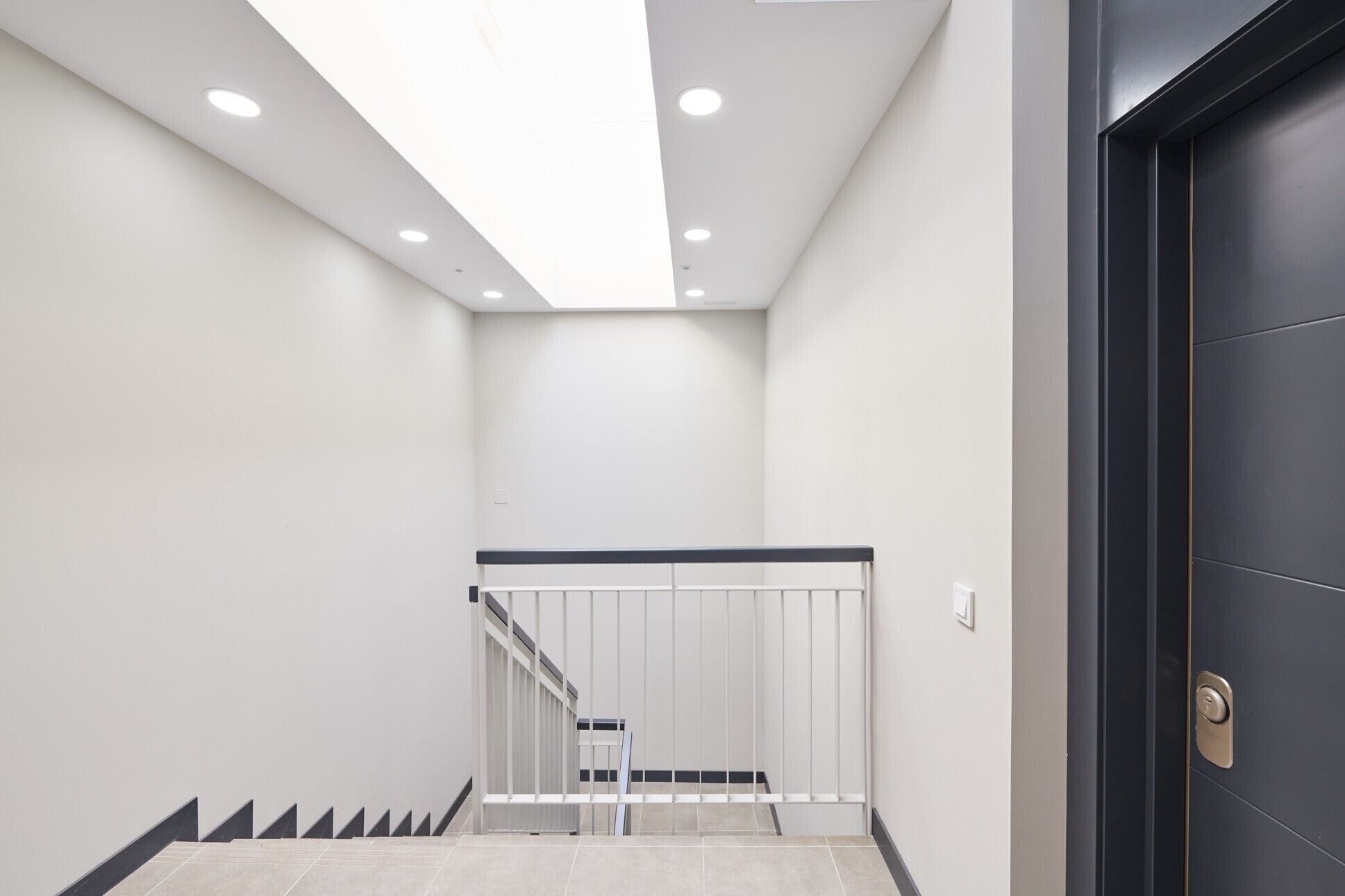 Un interior moderno con una escalera, una puerta negra e iluminación empotrada en el techo.