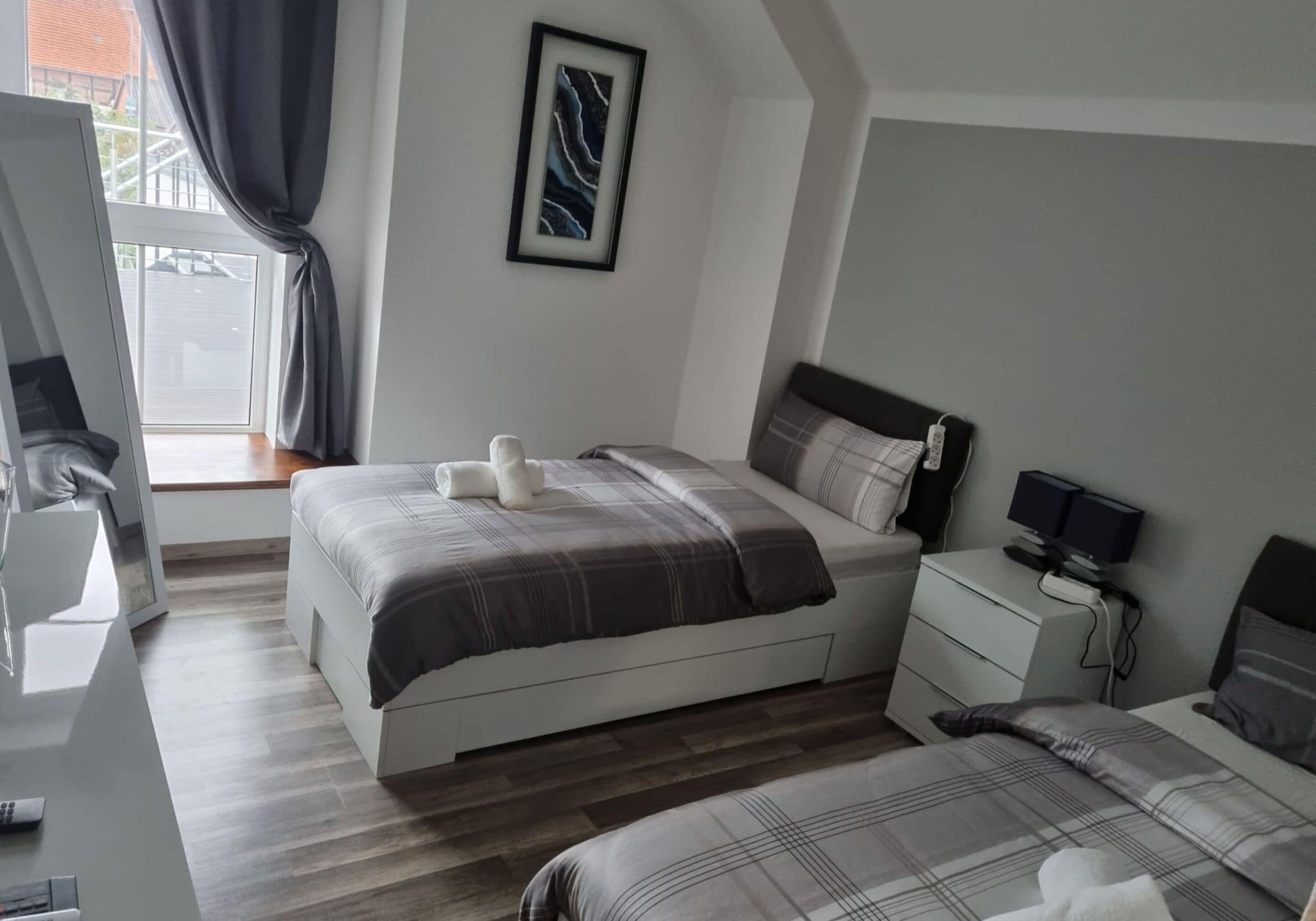 A modern hotel room with a large bed, a bedside table with a lamp, a small desk, and a window with curtains.