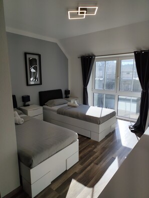 A modern bedroom with two beds, a large window with curtains, a ceiling light fixture, and a framed picture on the wall. - Gästezimmer Sarstedt (Sarstedt)