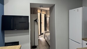 Una habitación de hotel moderna con televisión de pantalla plana, escritorio, lámpara, cama y refrigerador.