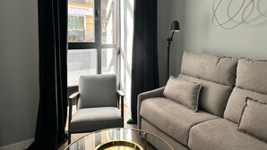 A modern living room with a sofa, armchair, and a glass coffee table. - PlazaMayorSuites Ext PARQUE DEL OESTE (Madrid)