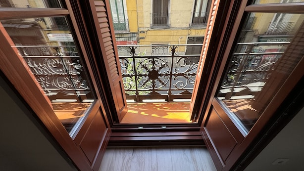 Blick von einem Balkon mit Metallgeländer auf eine Straße mit Gebäuden und einem Schild für "Bocadillo".