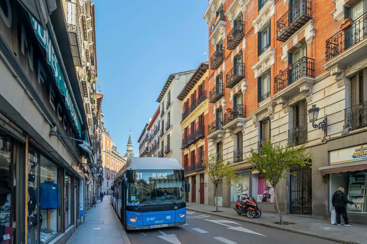 A narrow street with a blue bus labeled '31 Aluche' approaching.