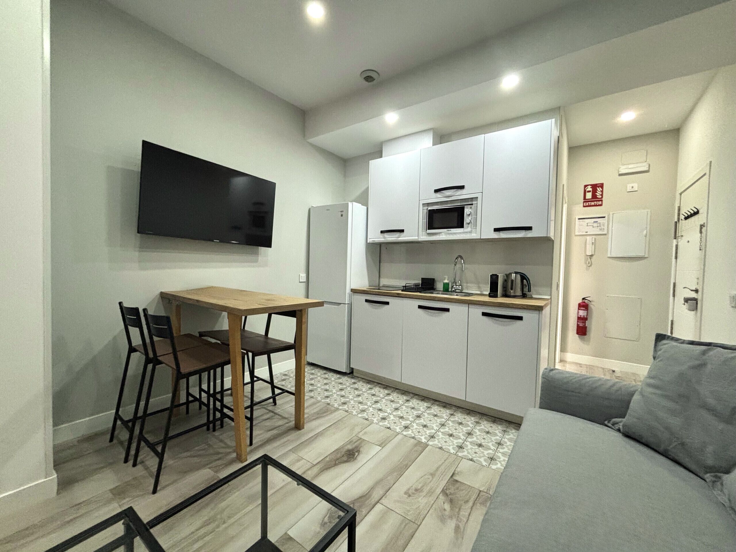 A compact kitchen with a dining area, a flat-screen TV, a refrigerator, a microwave, and a coffee maker.