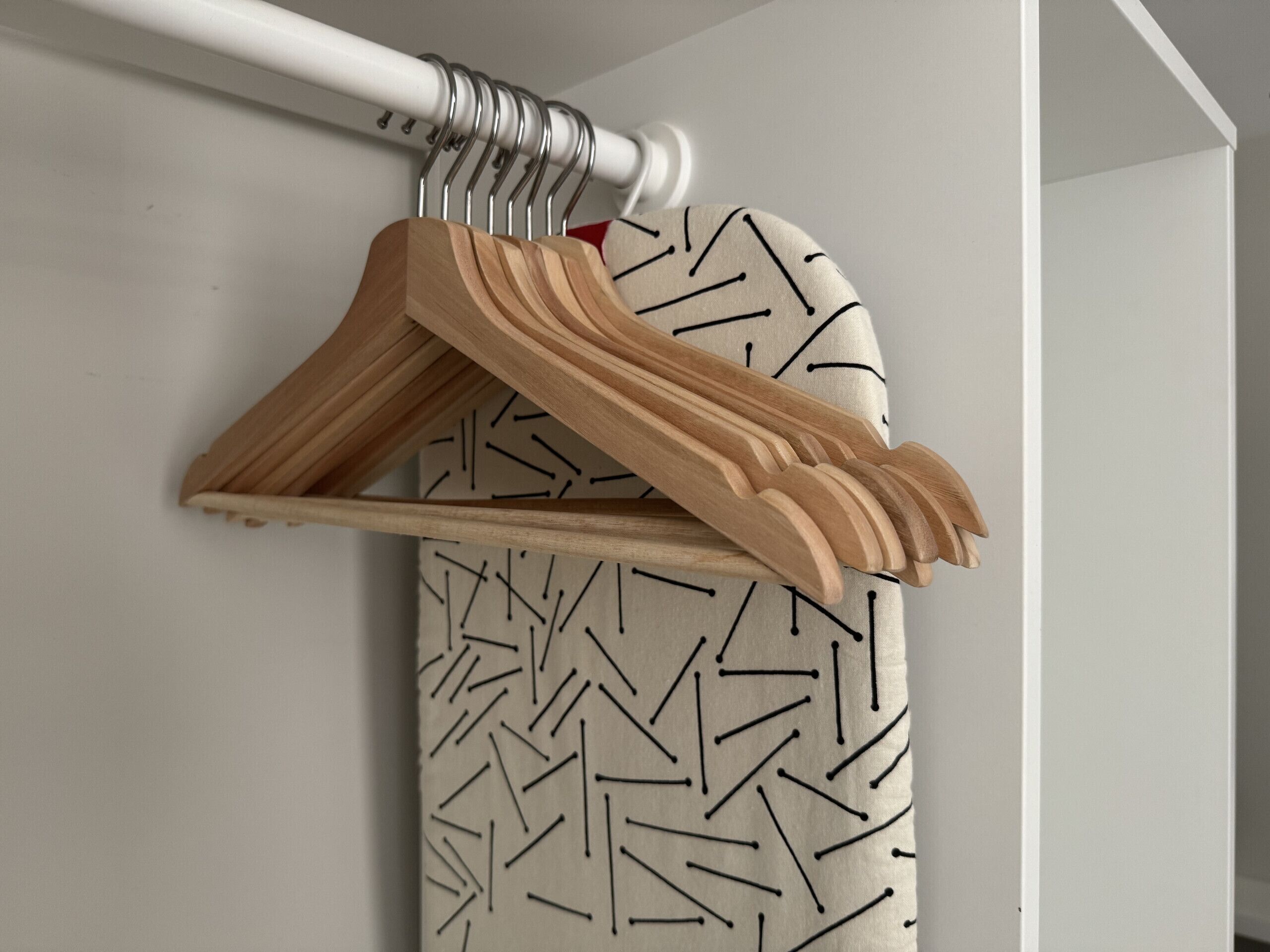 A wooden hanger rack with multiple hangers against a wall with a geometric pattern.