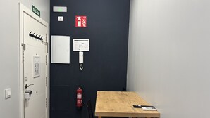 Una habitación con una mesa de madera, una silla, un extintor, un teléfono montado en la pared y una puerta con un letrero que indica una salida.