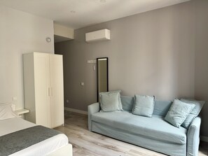 A bedroom with a bed, a wardrobe, a light-colored sofa, and a mirror.