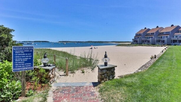 A beach with a sign detailing private beach rules, a stone pathway leading to the beach, and a row of houses in the background. - Oceanfront 3BR condo. 1600 sq ft of extended stay! Weekly and Monthly discounts! (Barnstable)