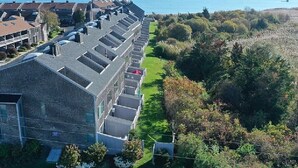 A row of modern, two-story buildings with a flat roof, arranged in a linear fashion along a green, tree-lined path. - Oceanfront 3BR condo. 1600 sq ft of extended stay! Weekly and Monthly discounts! (Barnstable)