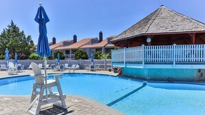 A swimming pool with lounge chairs and umbrellas, a covered seating area, and a building with a tiled roof. - Oceanfront 3BR condo. 1600 sq ft of extended stay! Weekly and Monthly discounts! (Barnstable)