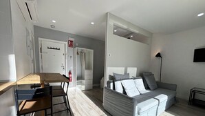A modern living room with a sofa, a dining table with chairs, and a kitchenette area.