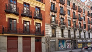 A row of red brick buildings with balconies, numbered 33, and storefronts with visible signage.