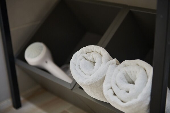 A bathroom with a towel rack holding two rolled towels and a hairdryer.