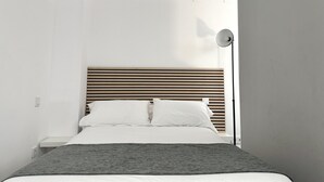 A modern bedroom with a wooden slatted headboard, white bedding, and a grey throw blanket.