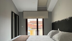 A hotel room with a large bed, a view of buildings through the window, and a ceiling light.