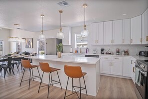 A modern kitchen with white cabinets, a large island with bar stools, pendant lighting, and a built-in oven.