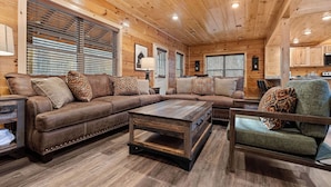 A cozy living room with a brown leather sectional sofa, a wooden coffee table, and a green armchair. - Welcome to Happy Holler Hideaway (Pigeon Forge)