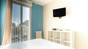 A hotel room with a large bed, a white console table, a mounted TV, and a window with curtains.