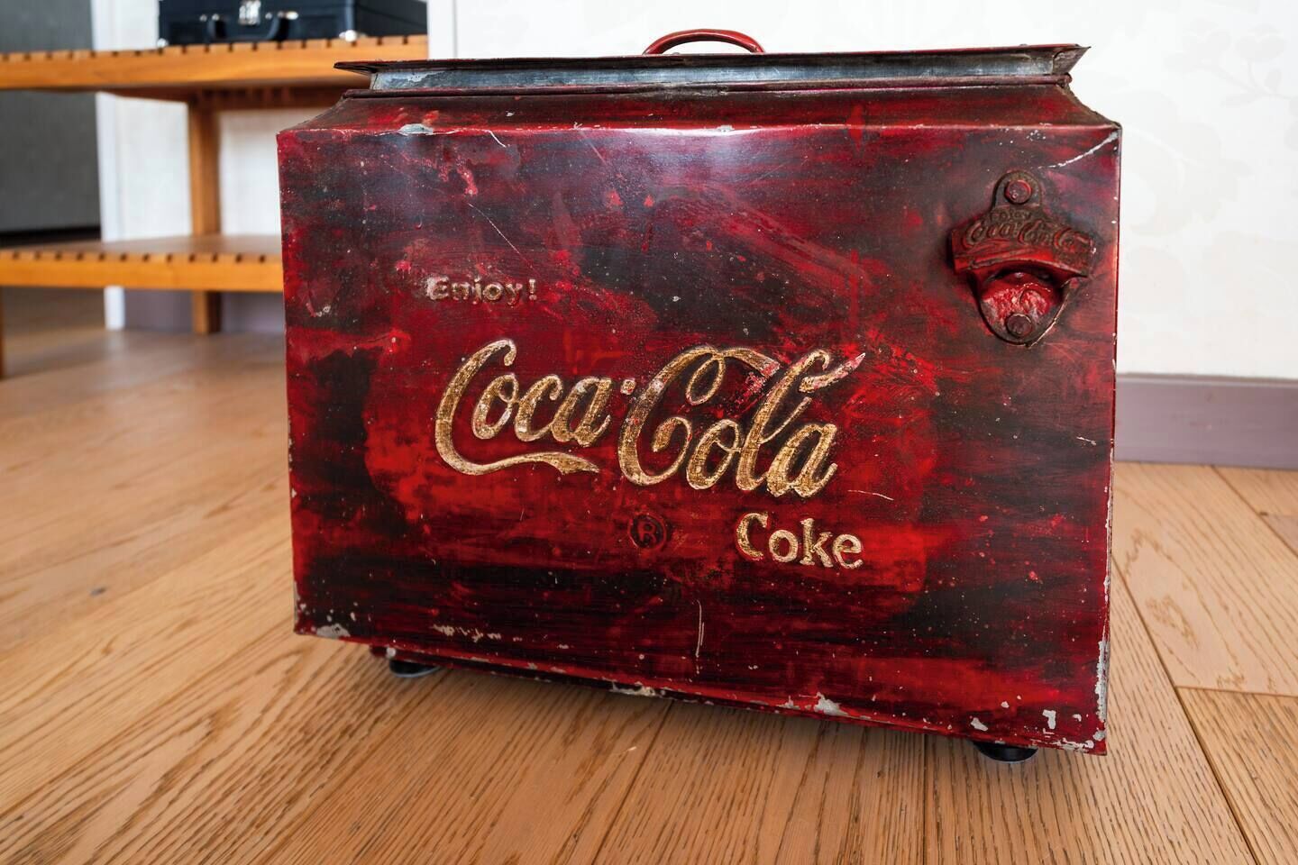 Un ancien réfrigérateur Coca-Cola, de couleur rouge à l’extérieur et orné de lettres dorées, est posé sur un plancher en bois.