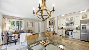 A spacious kitchen with modern appliances, a dining area with a glass table, and a living room with a sofa and a lamp. - Relaxing Coastal Getaway • 1st-Floor + Pool Access (Hilton Head Island)