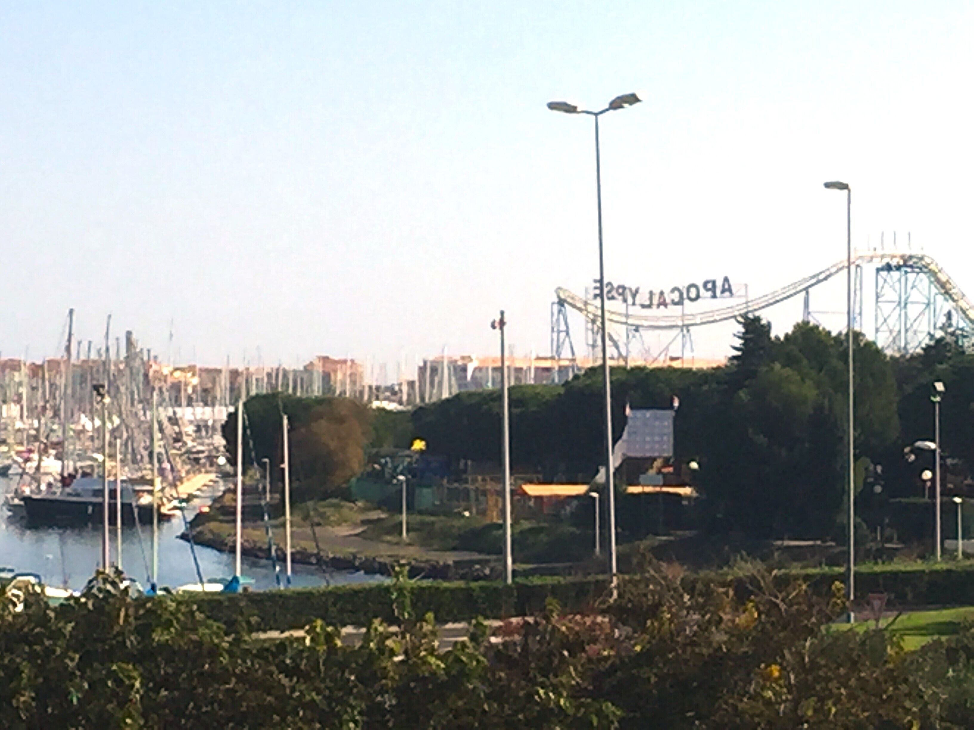 A coastal marina with boats, a roller coaster, and a clear sky.