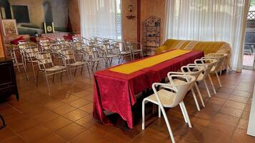 Uma sala de jantar com uma mesa comprida coberta por um lençol vermelho, rodeada por cadeiras brancas.