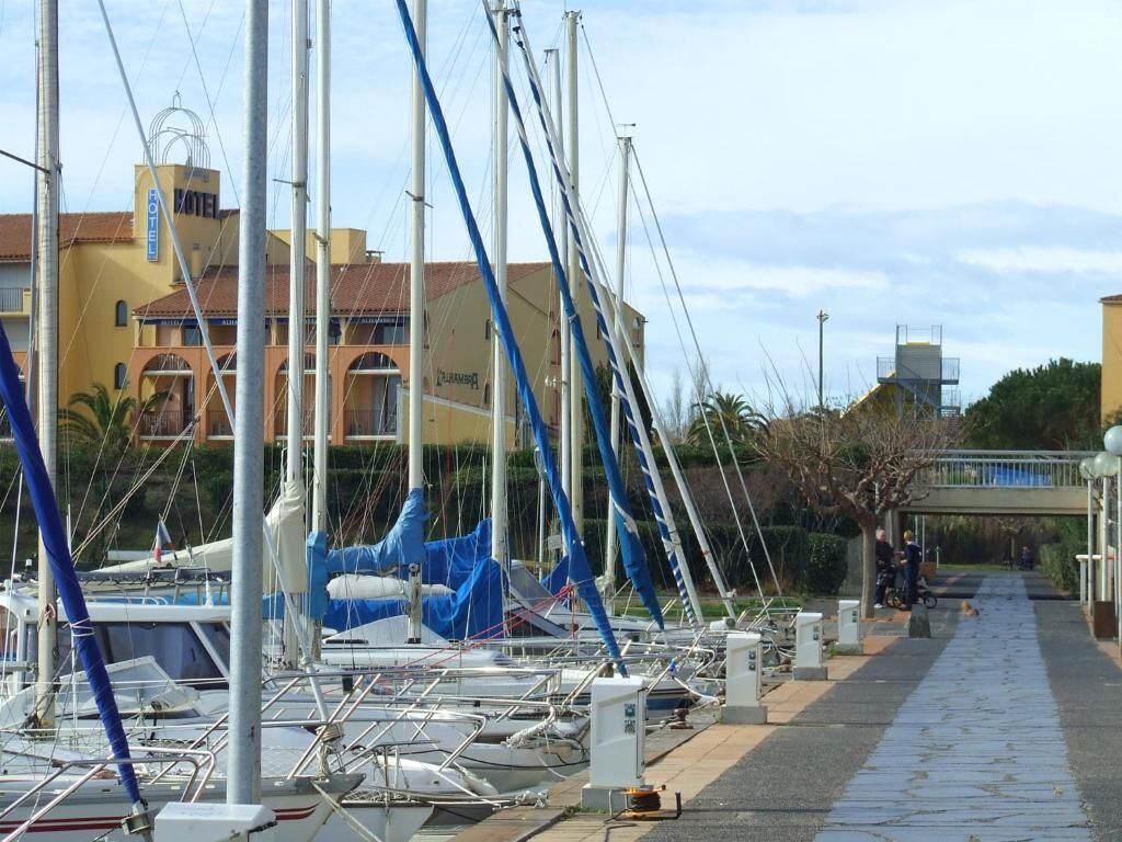 Ein Yachthafen mit mehreren Segelbooten, ein Hotel im Hintergrund und ein Fußweg.