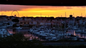 Un puerto deportivo con numerosas embarcaciones amarradas, una noria al fondo y edificios a lo largo del paseo marítimo.