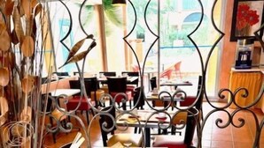 Un interior de restaurante con una zona de comedor central, mesas, sillas y un arreglo de plantas decorativo.
