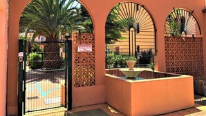 Una entrada con reja, ventanales arqueados y una fuente de agua.