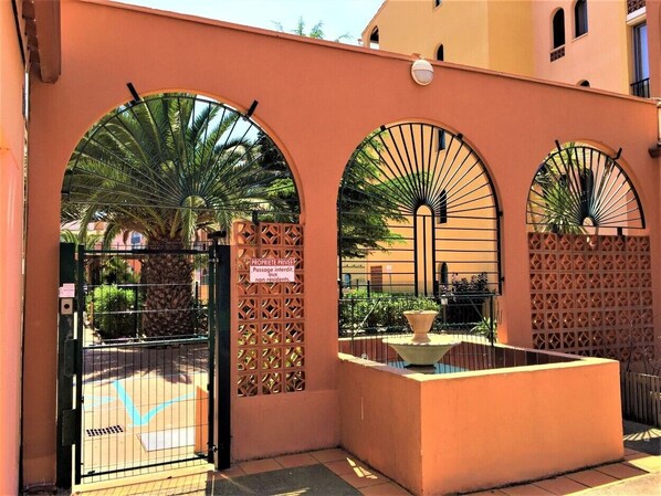 A gated entrance with arched windows and a water feature. - HÔTEL ALHAMBRA (Agde)