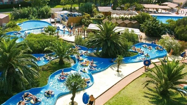 Parque acuático con múltiples toboganes y piscinas, rodeado de palmeras y una zona junto a la piscina con sombrillas.