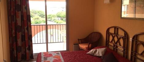 A bedroom with a bed, a chair, a balcony with a view, and a ceiling fan.