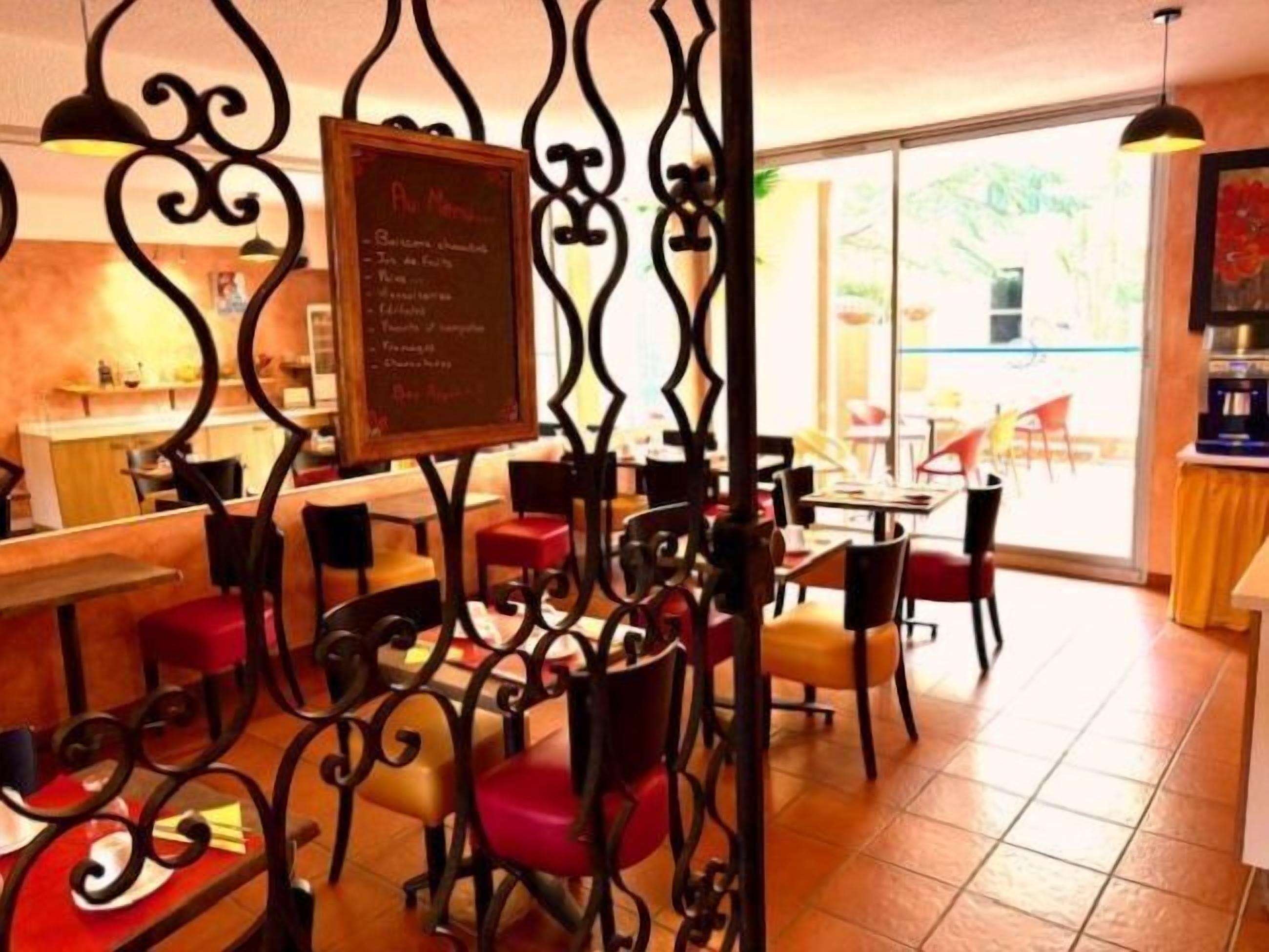 Interior de un restaurante con un menú en pizarra, sillas rojas y negras, y piso de baldosas.