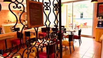 Interior de un restaurante con un menú en pizarra, sillas rojas y negras, y piso de baldosas.