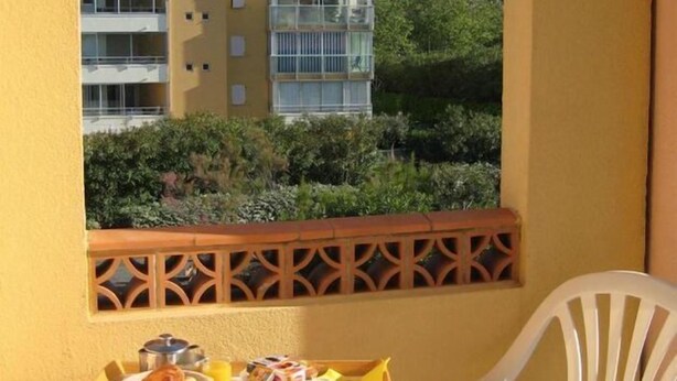 Un balcón con una mesa dispuesta para el desayuno, vista a un edificio y una barandilla decorativa.