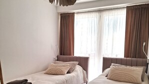 A hotel room with two beds, each with a pillow and a folded towel. There is a window with curtains and a pendant light above the beds. - Modern flat +2  pools on roof top! (Salou)