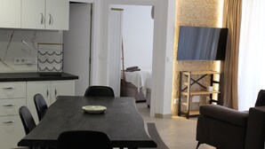 A modern hotel room with a dining area, a sofa, a TV mounted on a stone wall, and a bed in the background. - Modern flat +2  pools on roof top! (Salou)