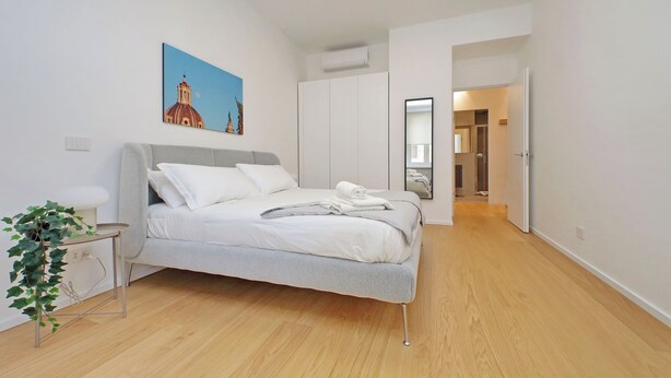 Un dormitorio moderno con una cama, una mesita de noche, una planta y un cuadro en la pared.