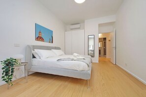 A modern bedroom with a bed, a bedside table, a plant, and a painting on the wall.