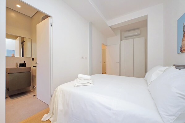 A hotel room with a bed, a bathroom with a sink and mirror, and a door leading to another room.
