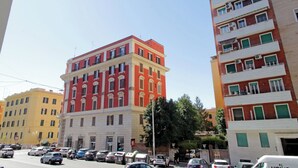 Un edificio de varios pisos con fachada roja y amarilla, varios balcones y un estacionamiento con automóviles.
