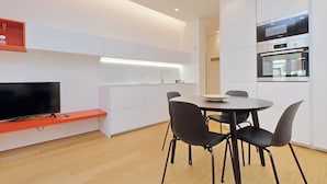 Una cocina moderna con electrodomésticos integrados, un comedor con una mesa redonda y sillas, y un televisor montado en un estante rojo.